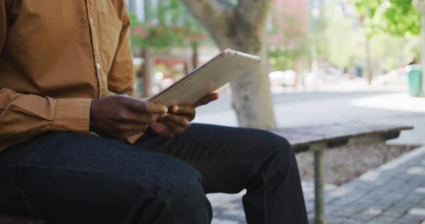 Midsection of african american businessman putting tablet in bag sitting on bench — Stock Video