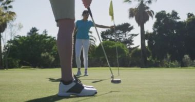 İki beyaz kadın golf oynuyor. Yüz maskesi takıyorlar. Biri sığınaktan ateş ediyor.