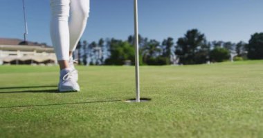 Beyaz kadın golfçü golf sahasında duran topa uzanıyor.