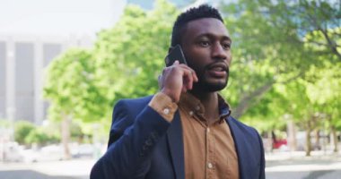 Afro-Amerikalı işadamı şehir caddesinde akıllı telefon kullanıyor.