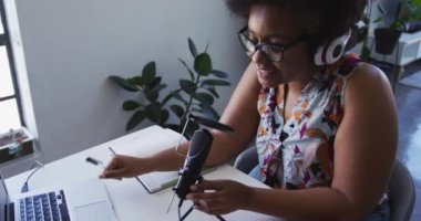 Afrika kökenli Amerikalı kadın ve kulaklık takan bir vlogger mikrofon kullanarak video blogu kaydediyor.