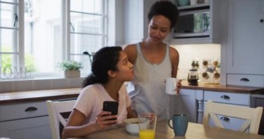 Karışık ırk lezbiyen çifti mutfakta sarılıyor ve kahve içiyor. Coronavirus covid 19 salgını sırasında evde tek başına vakit geçirmek..