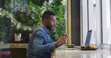 Afro-Amerikalı iş adamı laptopunu kafede kahve içerken kullanıyor. Haberleşme işi şehir dışına seyahat ediyor..