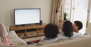 Karışık ırk lezbiyen çifti ve kızı kanepede oturmuş televizyon seyrediyor.