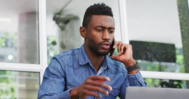 Afrika kökenli Amerikalı iş adamı akıllı telefondan konuşuyor ve laptopunu, kafesini, otobüsünü kullanıyor.