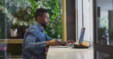Afro-Amerikalı iş adamı laptopunu kafede kahve içerken kullanıyor.