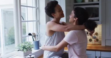 Karışık ırk lezbiyen çifti mutfakta sarılıyor ve kahve içiyor. Coronavirus covid 19 salgını sırasında evde tek başına vakit geçirmek..