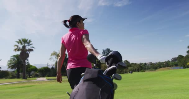 Белая женщина играет в гольф с сумкой, заполненной клюшками для гольфа — стоковое видео