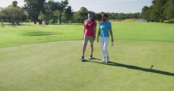Dos mujeres caucásicas jugando al golf usando mascarillas caminando juntas — Vídeo de stock