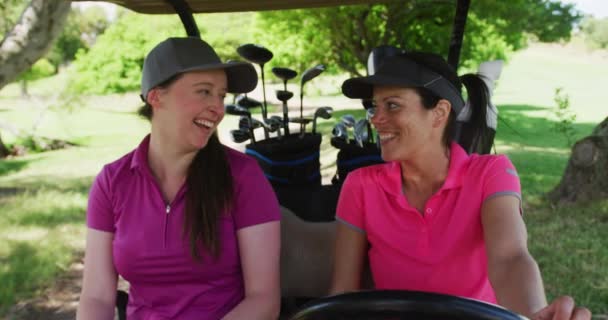 Δύο καυκάσιες γυναίκες που παίζουν γκολφ πάνω σε αμαξάκι του γκολφ μιλώντας και γελώντας. — Αρχείο Βίντεο