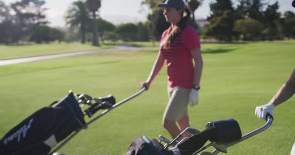 Dos jugadoras de golf caucásicas caminando con sus carros de kit de golf en el campo de golf — Vídeos de Stock