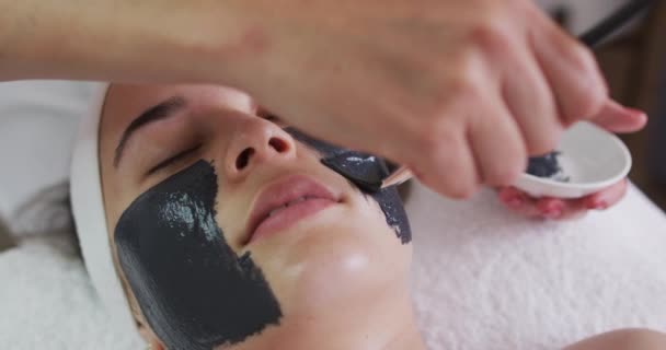 Mulher caucasiana deitada enquanto esteticista lhe dá uma máscara facial — Vídeo de Stock