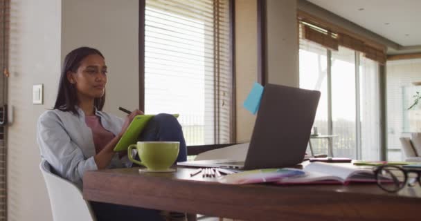 Mujer de raza mixta utilizando la escritura portátil en portátil beber café trabajando desde casa — Vídeos de Stock