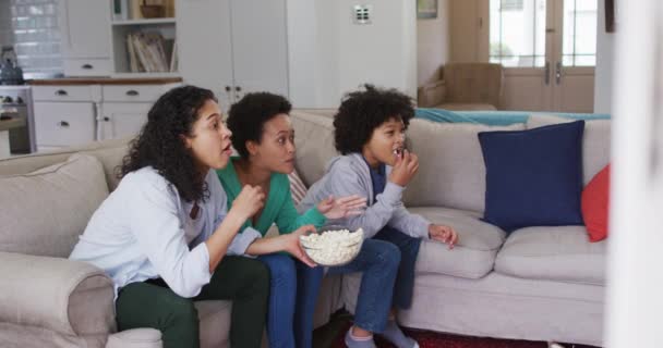 Μικτή φυλή λεσβιακό ζευγάρι και η κόρη βλέποντας τηλεόραση τρώει ποπ κορν — Αρχείο Βίντεο