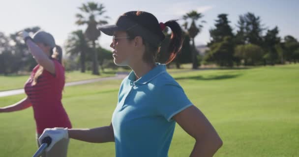 Dos jugadoras de golf caucásicas con carros de kit de golf hablando entre sí en el campo de golf — Vídeos de Stock