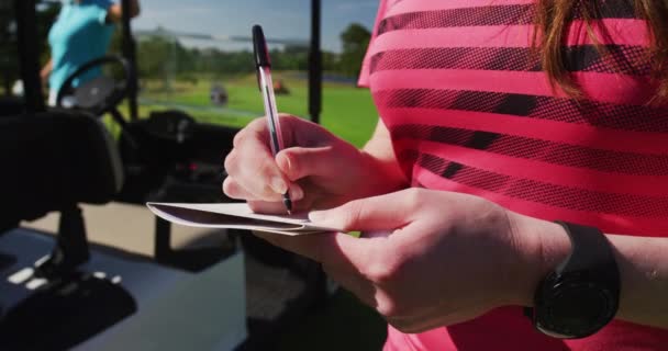 Duas mulheres caucasianas jogando golfe uma escrita em um caderno — Vídeo de Stock