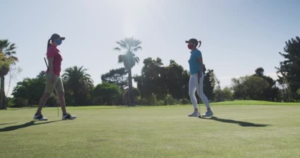 Duas mulheres caucasianas jogando golfe usando máscaras faciais cumprimentando uns aos outros com os pés — Vídeo de Stock