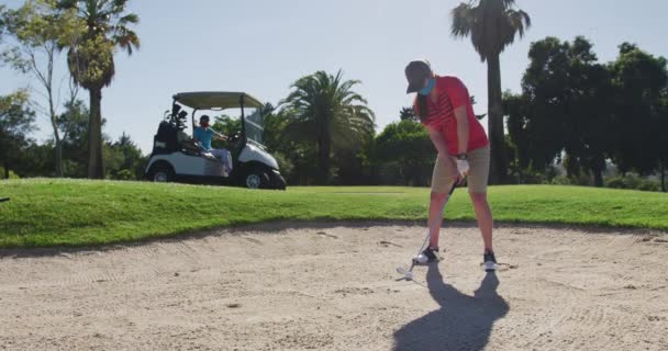 Duas mulheres caucasianas jogando golfe usando máscaras um tiro de bunker — Vídeo de Stock