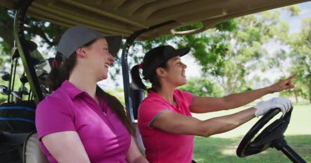 Dos mujeres caucásicas jugando al golf montando un carrito de golf hablando y riendo — Vídeos de Stock