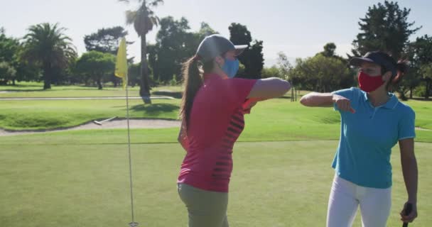 Dos mujeres caucásicas jugando al golf usando máscaras faciales saludándose con los codos — Vídeos de Stock