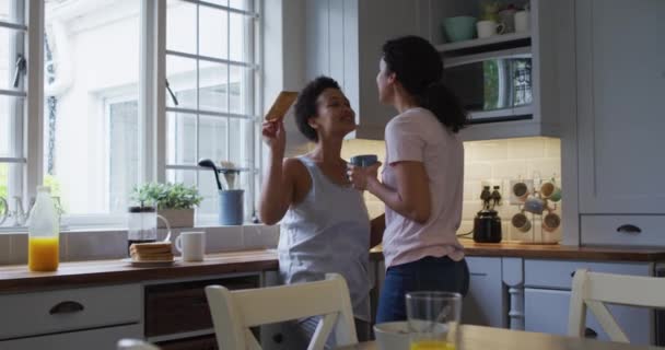 キッチンでは 男女混合のレズビアンカップルがコーヒーを飲んでいます 家庭での自己分離の質家族の時間コロナウイルスCovid 19パンデミックの間 — ストック動画