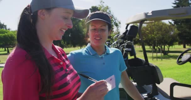 Две кавказки играют в гольф, одна пишет в блокноте. — стоковое видео