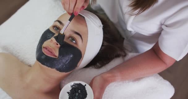 Mulher caucasiana deitada enquanto esteticista lhe dá uma máscara facial — Vídeo de Stock