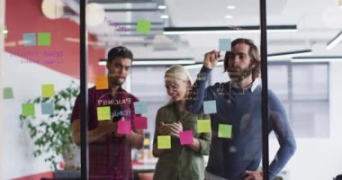 Çeşitli ofis arkadaşları cam tahtaya yazı yazıyor ve modern ofiste tartışıyorlar.