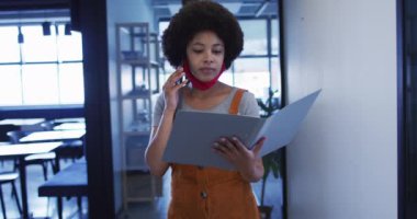 Karışık ırk işkadını maske takıyor modern ofiste evrak işleriyle uğraşıyor.