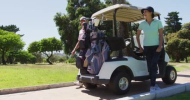 Kafkasyalı yaşlı çift golf sahasında golf arabasının arkasından golf sopalarını kaldırıyor. emeklilik sporları ve aktif yaşlı yaşam tarzı.