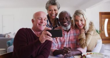 Masanın başında oturan, şarap içen, yemek yiyen ve selfie çeken farklı yaşlı çiftler. Huzurevinde sağlık hizmetleri.