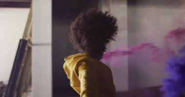 Melez bir kadın elinde mavi ve mor fişekler boş bir binada dans ediyor.