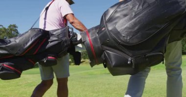 Golf sahasında golf çantalarıyla yürüyen yüz maskesi takan iki Kafkasyalı son sınıf öğrencisi. Coronavirus covid 19 salgını sırasında emeklilik sporları ve aktif yaşlı yaşam tarzı.