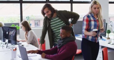 Modern ofiste çeşitli iş adamları dizüstü bilgisayar kullanarak konuşuyor.