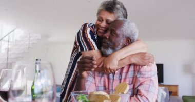 Afro-Amerikan son sınıf çifti masada oturmuş şarap içiyor, yemek yiyor ve sarılıyorlar. Huzurevinde sağlık hizmetleri.
