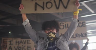 Yüz maskesi takan ve protesto işaretleri tutan bir grup insan.