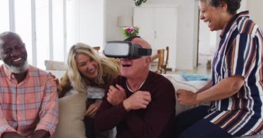 Kanepede oturan iki farklı kıdemli çift beyaz bir adam VR Google kullanıyor. Üst düzey emeklilik hayatı arkadaşları sosyalleşiyor.