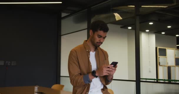 Uomo d'affari di razza mista in piedi utilizzando uno smartphone in un ufficio moderno — Video Stock