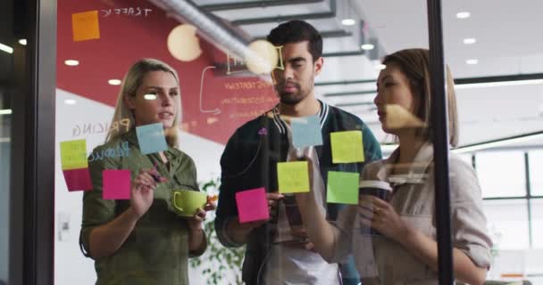 ガラス板に書き込み 現代のオフィスで一緒に議論する多様なオフィスの同僚 職場のコンセプトにおける団結とチームワーク — ストック動画