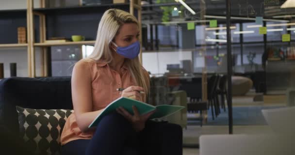 Empresários caucasianos usando máscaras faciais sentados passando por papelada no escritório moderno — Vídeo de Stock