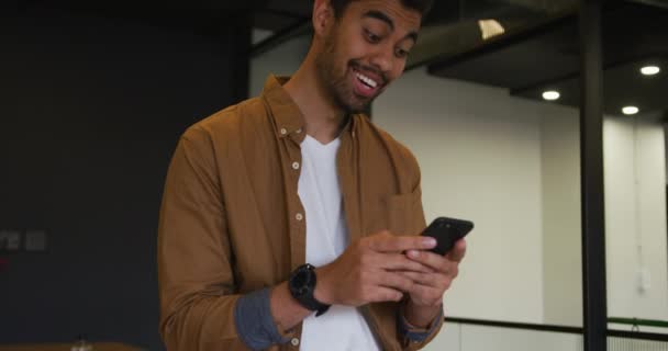 Mieszany biznesmen wyścigowy stojący przy użyciu smartfona w nowoczesnym biurze — Wideo stockowe