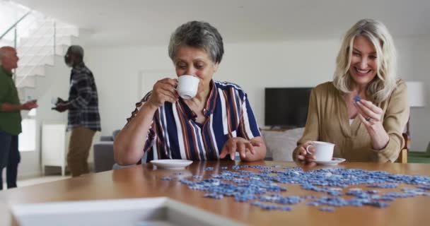 Afrikanische Und Kaukasische Seniorinnen Sitzen Tisch Und Rätseln Und Trinken — Stockvideo