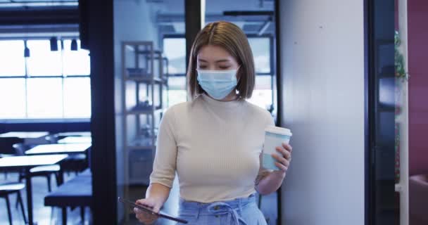 현대 사무실에서 디지털 태블릿으로 마스크를 착용하고 걷고 있는 아시아 여성 — 비디오