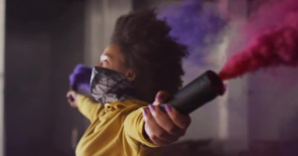 Femme de race mixte tenant des fusées éclairantes bleues et violettes debout dans un bâtiment vide — Video
