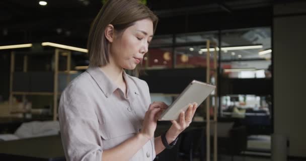 Empresária asiática de pé usando um tablet digital em um escritório moderno — Vídeo de Stock