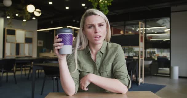Кавказская деловая женщина в видеочате пьет чашку кофе в современном офисе — стоковое видео