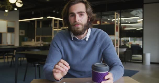 Kaukasischer Geschäftsmann bei einem Videochat mit einer Tasse Kaffee im modernen Büro — Stockvideo