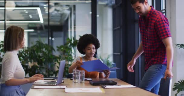 Divers gens d'affaires assis en utilisant un ordinateur portable passant par la paperasserie dans le bureau moderne — Video