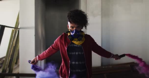 Hombre de raza mixta sosteniendo bengalas azules y púrpuras de pie en un edificio vacío — Vídeo de stock