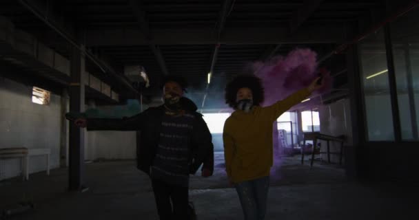 Mieszana rasa mężczyzna i kobieta trzymający niebiesko-fioletowe flary biegnące przez pusty budynek — Wideo stockowe